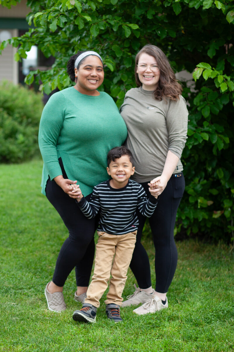 A child and two adults pose together in front of a large bush