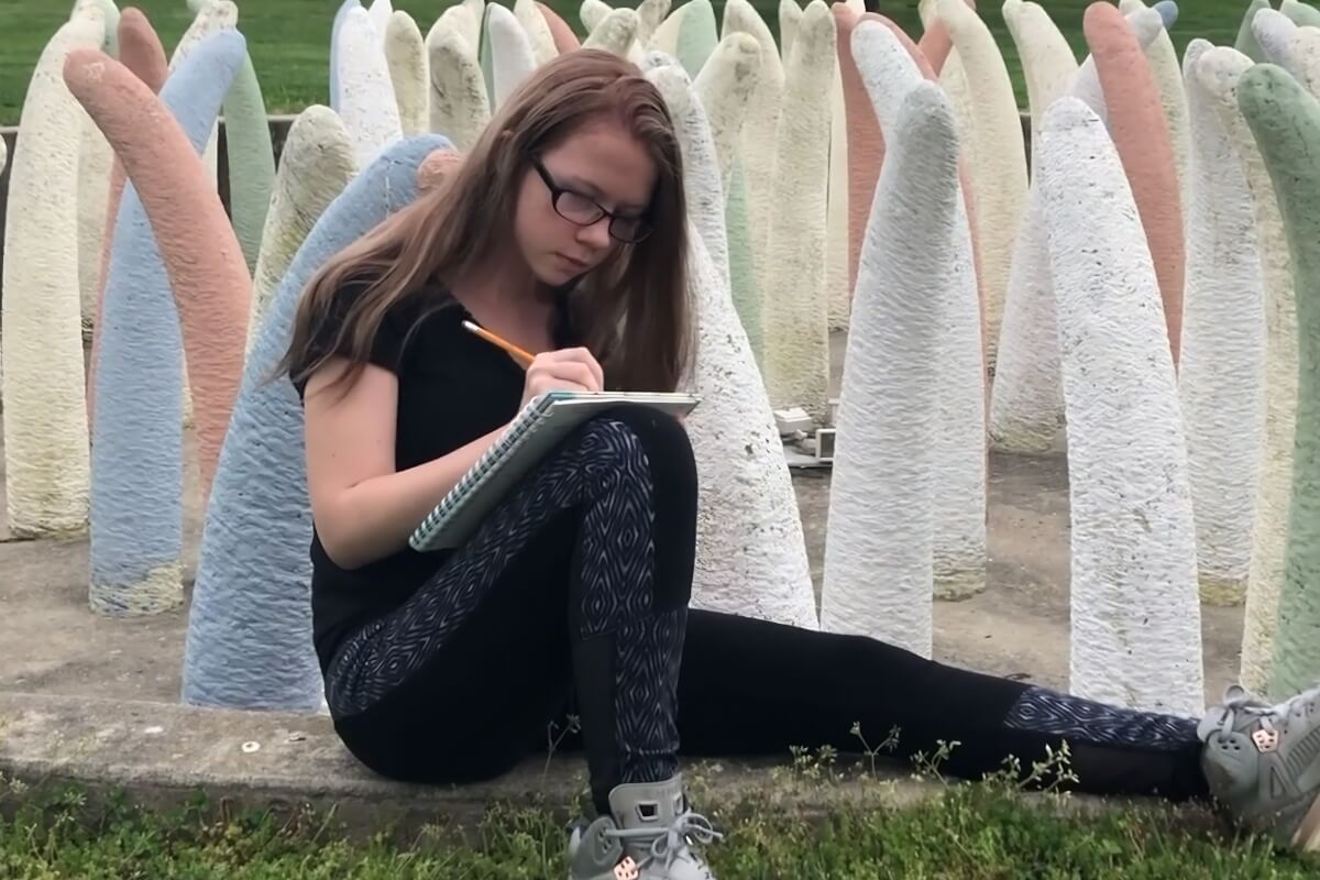 Young camper writing in a notebook while sitting outdoors