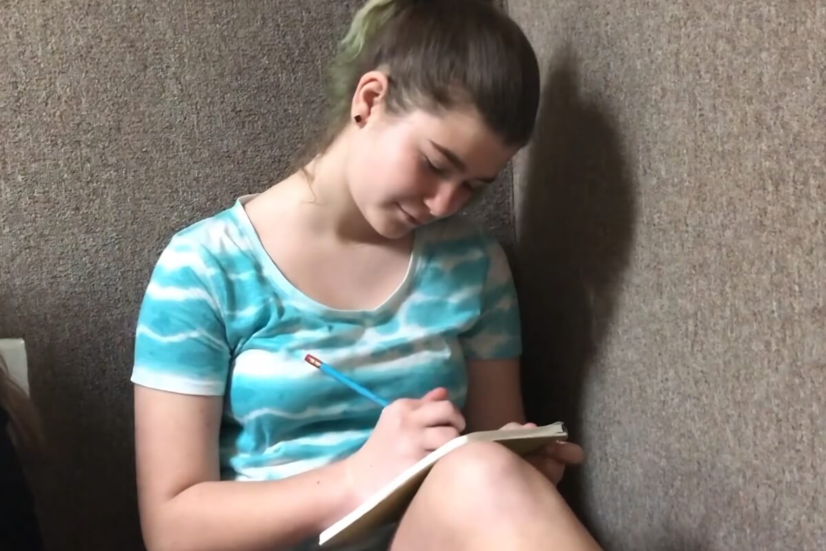Camper writing in a notebook with a pencil