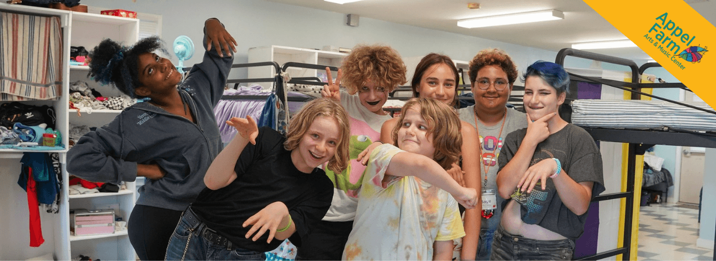 Group of campers smiling and posing, with bunk beds behind them in their cabin.
