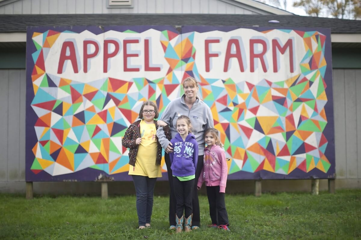 Adult and kids posed before an Appel Farm wall graphic.